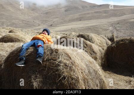 Das Kind liegt auf dem Heuballen auf dem Bauernhof, Kabardino-Balkarien, Russland Stockfoto