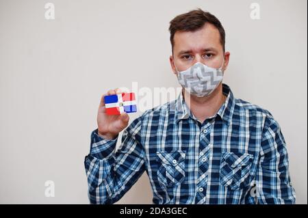 Mann im karierten Hemd zeigen Dominikanische Republik Flagge Karte in der Hand, tragen Schutzmaske isoliert auf weißem Hintergrund. Amerikanische Länder Coronavirus conce Stockfoto