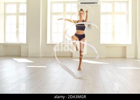 Athletische flexible Mädchen Turnerin führt Übungen mit einem Band in einem hellen Saal. Stockfoto