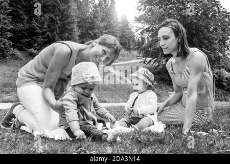Zwei Freundinnen genießen ein Picknick in einer schönen sonnigen Tag mit ihren kleinen Töchtern - Frauen sitzen mit kleinen Kleine Mädchen auf Gras im Berg Stockfoto