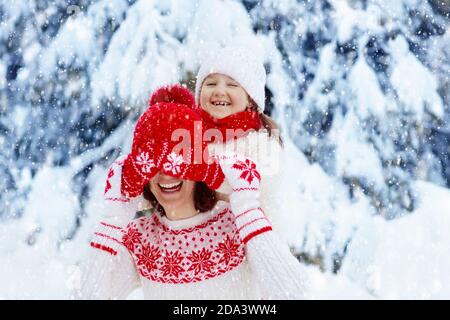 Mutter und Kind in gestrickten Wintermützen spielen im Schnee auf Familienweihnachtsferien. Handgemachte Wollmütze und Schal für Mama und Kind. Stricken für Kinder. Stockfoto