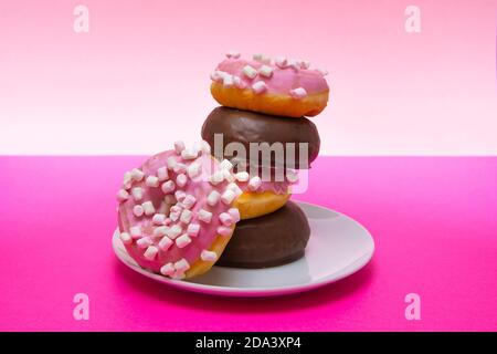 Nahaufnahme eines weißen Tellers rosa Donuts mit Kreuzkümmel und Schokolade bedeckt. Horizontale Fotografie Stockfoto