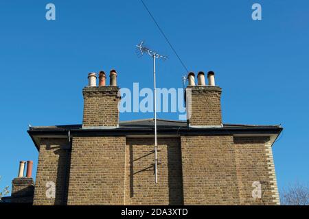 Eine fernsehantenne auf einem hohen Mast ragt zwischen Kaminen über der Ziegelmauer eines Hauses in twickenham, im Südwesten londons, england Stockfoto