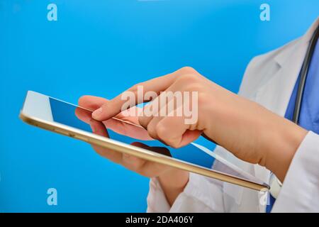 Der Arzt drückt seine Hand aus nächster Nähe auf den Tablet-Bildschirm. Krankenschwester nutzt das Internet, um Patienten zu helfen, blauer Hintergrund. Konzept, Patienten mit Witz zu helfen Stockfoto