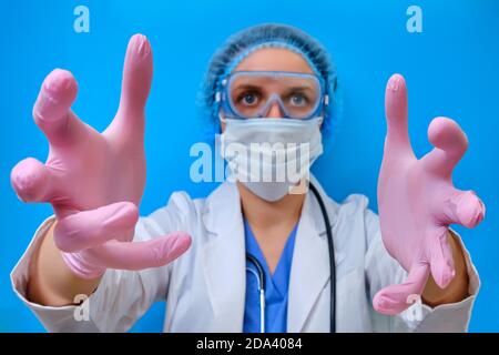 Gruselige Hände des Arztes, die sich wie im Delirium nach vorne zum Patienten streuten. Erschreckende Krankenschwester in medizinischen Handschuhen auf blauem Hintergrund, Nahaufnahme. Konzept e Stockfoto
