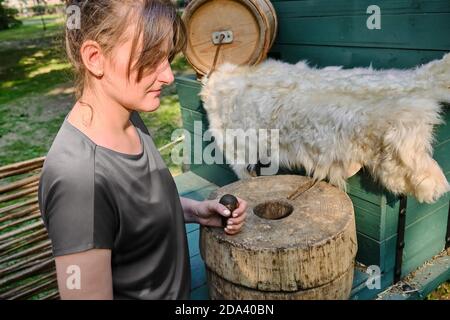 Die junge Frau mahlt Mehl mit Handmühlen. Retro Mühlstein zum Mahlen von Getreide und Mais Stockfoto