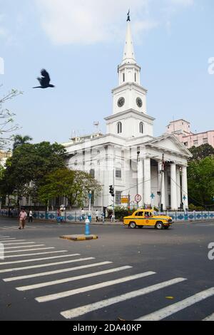 Kolkata, Indien - März 2014: Gelbe Taxi-Ambassador an der Kreuzung vor der alten katholischen St. Andreas-Kirche in Kalkutta Stockfoto