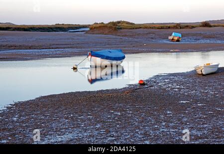 Ein Blick auf Overy Creek bei Ebbe mit kleinen Booten am Abend durch den North Norfolk Hafen von Burnham Overy Staithe, Norfolk, England, Vereinigtes Königreich. Stockfoto