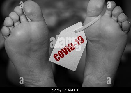 Nahaufnahme der Leichenfüßen im Leichenschauhaus auf dem Tisch mit der Aufschrift COVID-19. Pandemie, Coronavirus. Tragödie und Tod weltweit Stockfoto