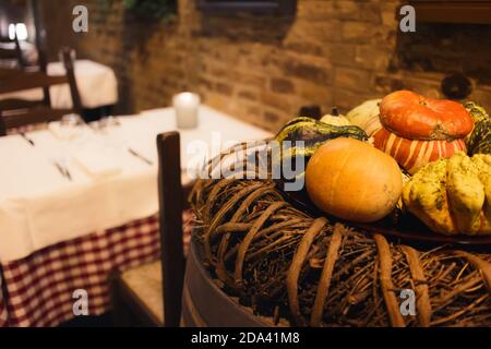 Dekorative Kürbisse in der Herbstsaison an den Tischen eines rustikaler italienischer Speisesaal mit vorbereiteten Tischdecken Stockfoto