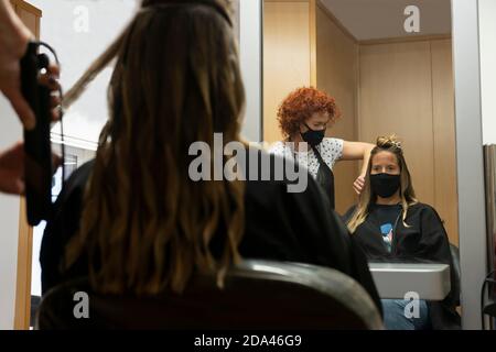 Professioneller Friseur, Stylist, der spezielle Frisur macht, lange schöne Haare aufrichten mit Haarbügeln im Schönheitssalon, in einem Spiegel reflektiert.WEA Stockfoto