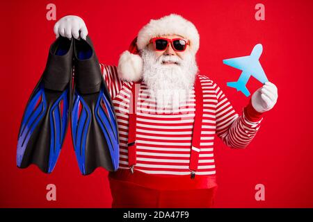 Foto von Großvater grauen Bart halten Papier Flugzeug Tauchausrüstung flippers tragen weihnachtsmann x-Mas Kostüm Hosenträger Sonnenschutz gestreiftes Hemd Kappe isoliert Stockfoto