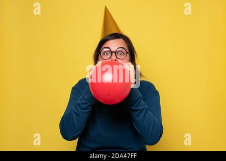 Kaukasische Frau in Partei Hut sprengen roten Ballon Stockfoto