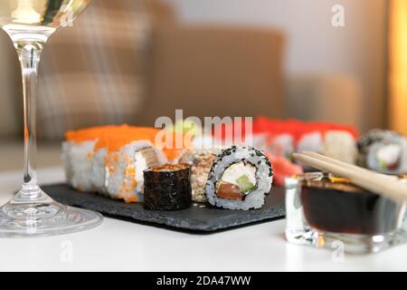 Ein Set aus farbenfrohem Sushi auf einem weißen Tisch mit Wein in einem gemütlichen Raum. Stockfoto