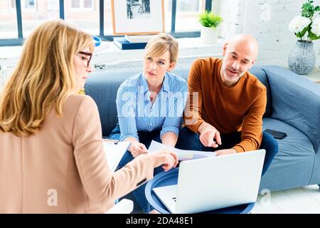 Glückliches Paar, das mit ihrem Finanzberater kommunizierte, während es zu Hause im Wohnzimmer saß. Stockfoto