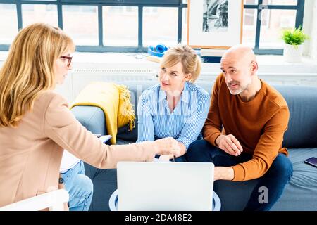 Glückliches Paar, das mit ihrem Finanzberater kommunizierte, während es zu Hause im Wohnzimmer saß. Stockfoto