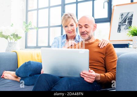 Aufnahme eines glücklichen Paares, das einen Laptop benutzt, während es sich auf dem Sofa zu Hause entspannt. Stockfoto