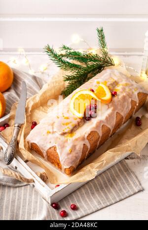 Weihnachtliche Orangenkuchen mit Preiselbeeren und Zuckerzuckerguss auf rustikalem Holzhintergrund. Feiertagsdekoration mit Festoon und Tannenzweig. Stockfoto