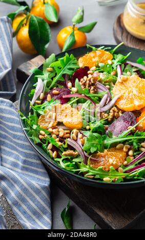 Frisch hausgemachter Mandarine- und Rübensalat mit Rucola, Walnüssen und Pinienkernen auf grauem Betongrund mit Dressing. Gesundes veganes Essen. Stockfoto