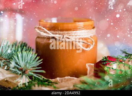 Ein kleines Glas mit gekochter, hausgemachter Kondensmilch. Shortbread Weihnachtsplätzchen, Lichter, Fichtenbrötchen, Unebenheiten. Inhalte für das neue Jahr. Stockfoto