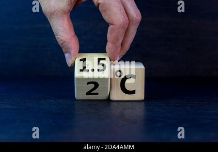 Symbol für die Begrenzung der globalen Erwärmung. Männliche Hand dreht einen Würfel und ändert den Ausdruck '2 C' in '1.5 C', oder umgekehrt. Konzept. Schönes dak Holz Stockfoto