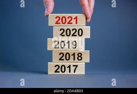 Männliche Hand, die einen Block mit der Nummer '2021' auf einen Turm mit den Nummern '2017, 2018, 2019, 2020' setzt. Schöner grauer Hintergrund. Speicherplatz kopieren. Unternehmen Stockfoto