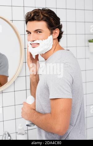Lächelnder Mann, der Rasierschaum im Badezimmer anhatte Stockfoto
