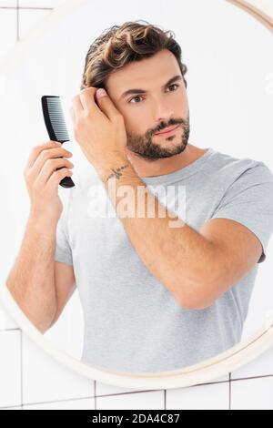 Brunette Mann Blick auf Spiegel beim Kämmen Haare im Badezimmer Stockfoto
