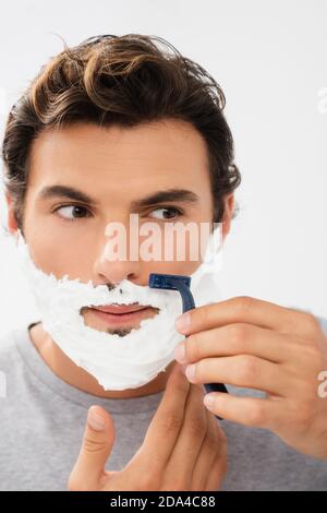 Junger Mann mit Schaum auf Gesicht Rasur mit Einweg-Rasierer Isoliert auf Grau Stockfoto