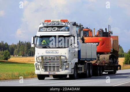 Weißer Volvo FH16 LKW schleppt Doosan Raupenbagger auf Anhänger entlang der Autobahn an einem Tag des Sommers. Luopajarvi, Finnland. August 2019. Stockfoto