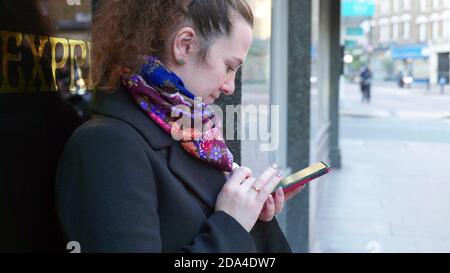 Frau, die in London auf der Straße steht und Smartphone benutzt england gb Stockfoto