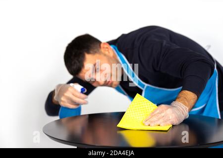 Junger Mann wischt den Tisch mit einem Lappen und hausgemachtem Spray. Geschlechterstereotypen. Foto auf weißem Hintergrund. Stockfoto