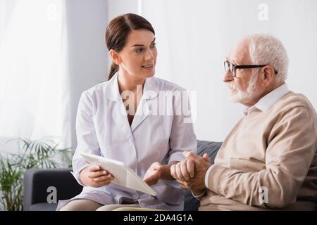 Sozialarbeiter mit digitalem Tablet und im Gespräch mit einem älteren Mann Sitzend mit geballten Händen Stockfoto