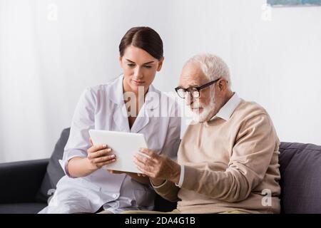 Brunette geriatrische Krankenschwester und ältere Mann mit digitalen Tablet zusammen Stockfoto