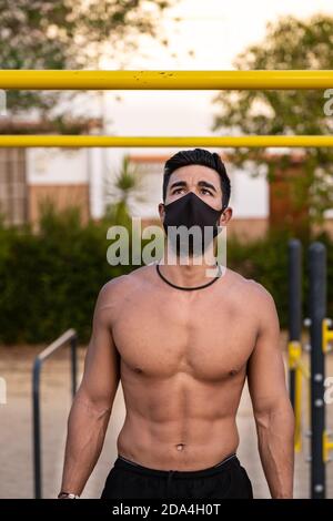 Junger Latino Mann in schwarzen Hosen und Maske macht Übungen In einem Calisthenics Park ohne T-Shirt Stockfoto