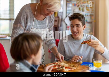 Mutter und Söhne essen zu Hause Pizza zum Mittagessen Stockfoto