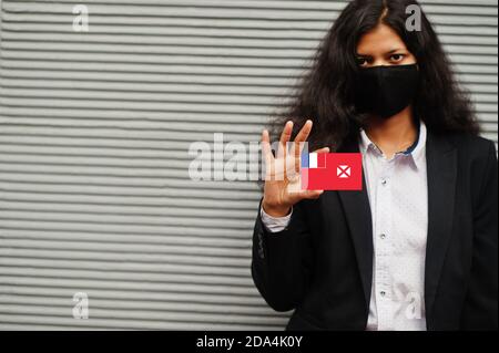 Asiatische Frau bei formeller Kleidung und schwarz schützen Gesichtsmaske halten Wallis und Futuna Flagge bei der Hand vor grauem Hintergrund. Coronavirus im Country-Konzept. Stockfoto