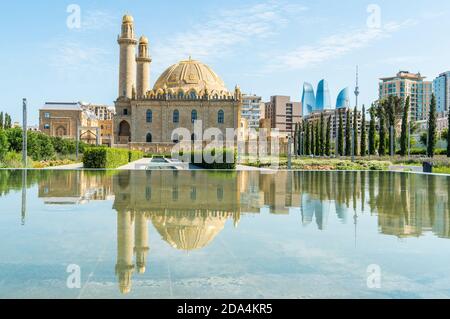 Baku, Aserbaidschan – 26. Juli 2020. Zwei Minaretten Teze Pir Moschee in Baku. Blick mit Reflexionen in einem Teich, mit Flame Towers Gebäuden und TV-Turm i Stockfoto