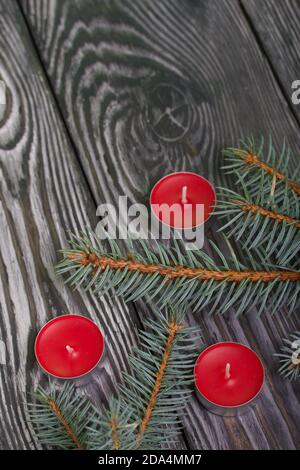 Äste aus blauer Fichte auf gebürsteten Kiefernholzplatten. In der Nähe gibt es rote Kerzen. Stockfoto