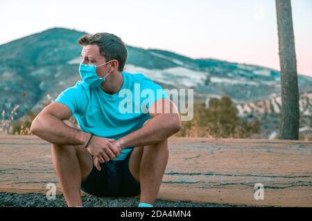 Porträt eines jungen kaukasischen Mannes, der in einem Park sitzt Blick auf den Horizont mit einer Maske Stockfoto