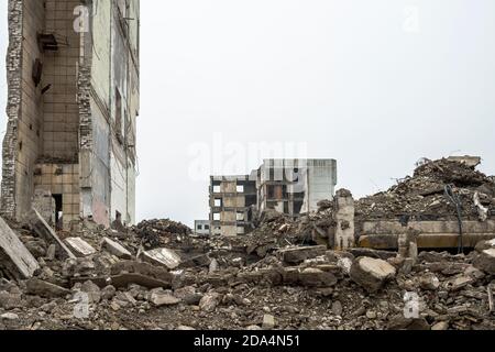 Ein zerstörtes Gebäude mit einem Haufen von grauen Betonschutt gegen einen neutralen grauen Himmel in einem Dunst. Hintergrund Stockfoto