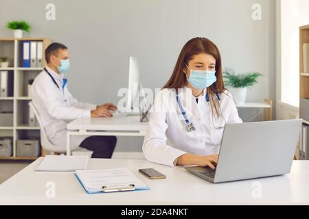 Ärzte in medizinischen Gesichtsmasken arbeiten auf Computern sitzen an Schreibtische im Büro Stockfoto