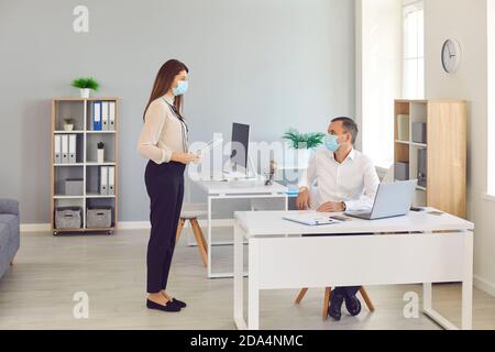 Büromitarbeiter, die Schutzmasken tragen, halten beim Kommunizieren im Büro Sicherheitsabstand ein. Stockfoto