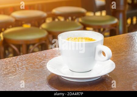 Weiße Tasse Kaffee auf einem Holztisch in einem Café, im Hintergrund Barhocker Stockfoto