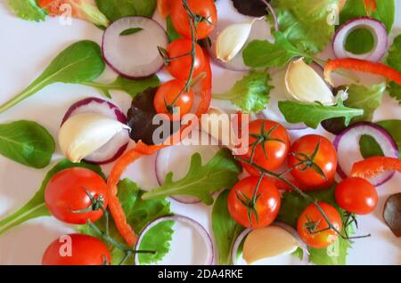 Bunte Salat Zutaten Muster aus Tomaten, Ruccola, lila Zwiebelringe, rote Paprika, Chili, Knoblauch, Gurkenscheiben und Basilikum auf weiß Stockfoto