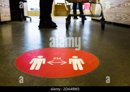 Rotes rundes Schild auf dem Boden an der Supermarkt-Kasse melden sie sich an, um Personen zu informieren, dass sie 2 Meter Abstand halten sollen Von einander, verhindern Ausbreitung Stockfoto