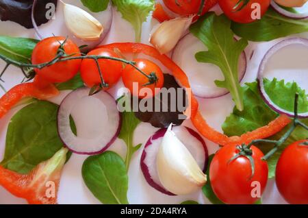 Bunte Salat Zutaten Muster aus Tomaten, Ruccola, lila Zwiebelringe, rote Paprika, Chili, Knoblauch, Gurkenscheiben und Basilikum auf weiß Stockfoto