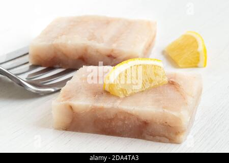 Zwei schnell gefrorene Fischfiletblöcke mit Zitronenkeilen und Metallspatel auf Weiß. Stockfoto