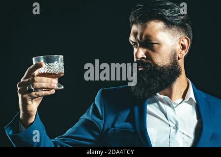 Selbstbewusster, gut gekleideter Mann mit einem Glas Whisky. Ernste traurige Frau, die Alkoholabhängigkeit hat. Mann, der Alkohol aus einem Glas trinkt. Stockfoto