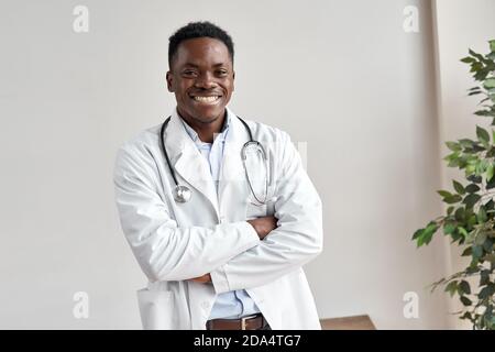 Glücklich afrikanischen männlichen Arzt Blick auf Kamera stehen an der weißen Wand. Stockfoto
